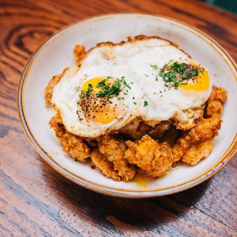 Close-up of fried chicken and two sunny-side-up eggs with chives.