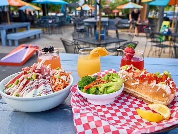 Colorful poke bowl, lobster roll, and drinks on an outdoor restaurant table.