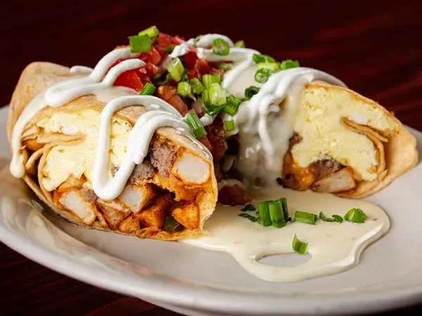 Halved breakfast burrito with eggs, potatoes, sausage, sauce, and pico de gallo.