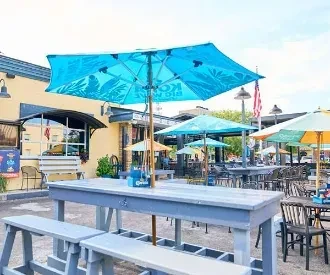 Turquoise Kona Big Wave umbrella shades an outdoor restaurant patio.