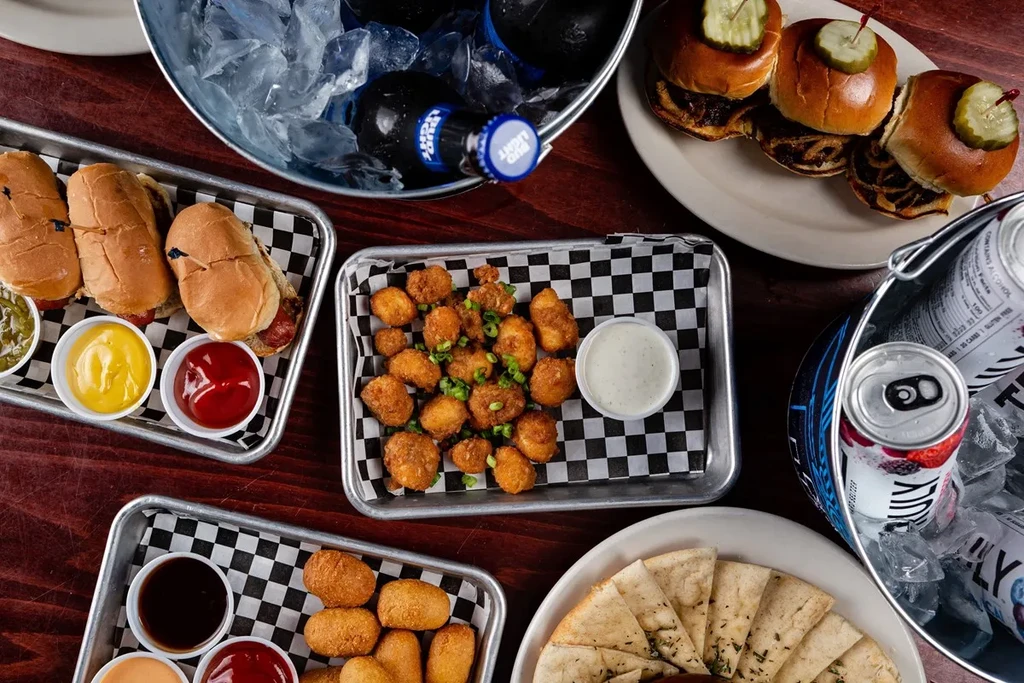 Overhead shot: table with fried foods, mini sandwiches, Bud Light, Truly.
