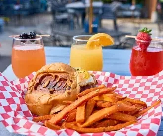 Savory bun, sweet potato fries, and three colorful garnished drinks outdoors.