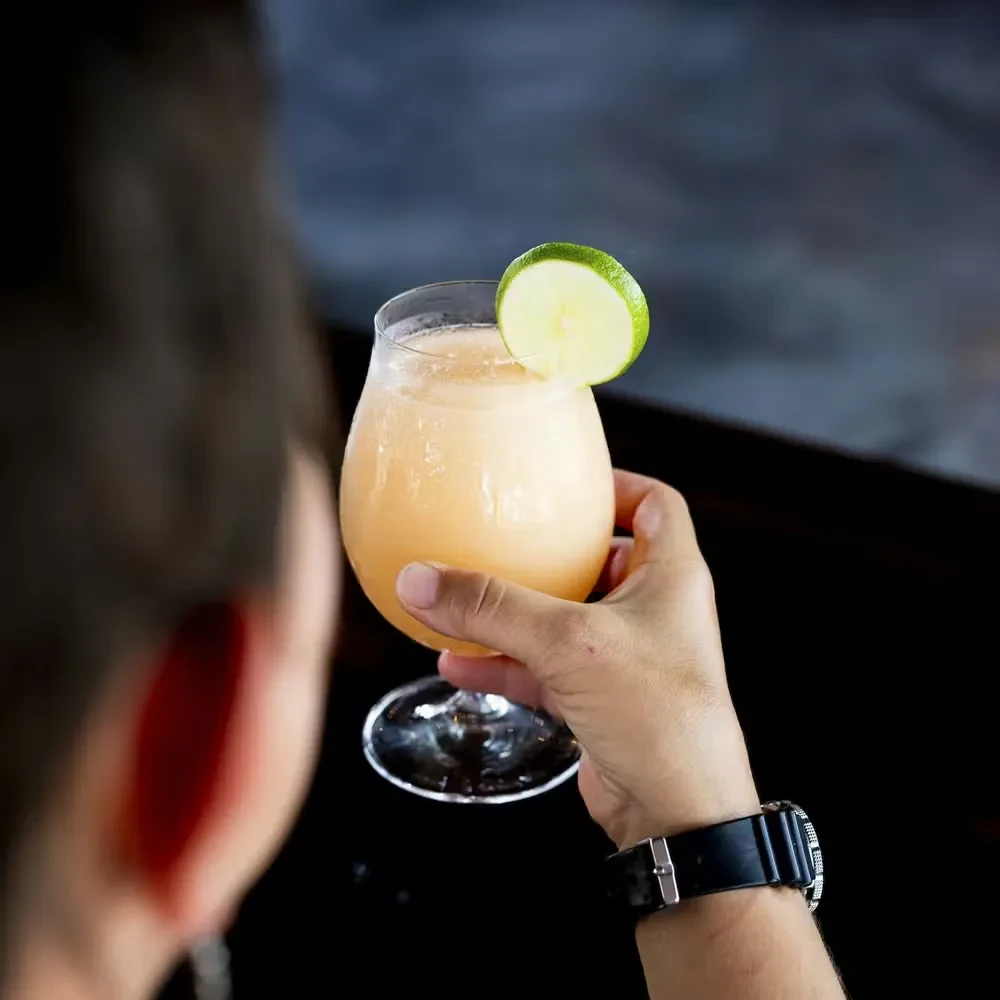 Hand holds frosty orange drink with lime in stemmed glass.