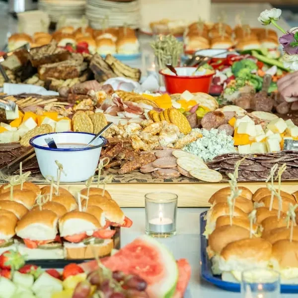 A vibrant buffet spread with charcuterie, fruit, sandwiches, and pastries.