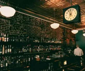 Dimly lit bar with liquor bottles on brick wall and ornate tin ceiling.