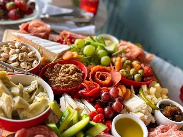 Vibrant charcuterie board with cheeses, folded meats, fresh fruits, and olives.