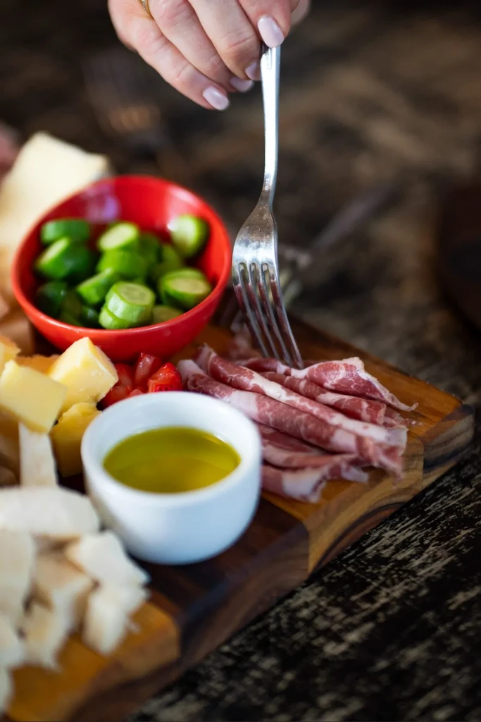 Hand with a fork reaching for cured meat on a charcuterie board.