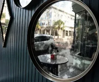 Large circular mirror on dark wall reflects urban street and table.