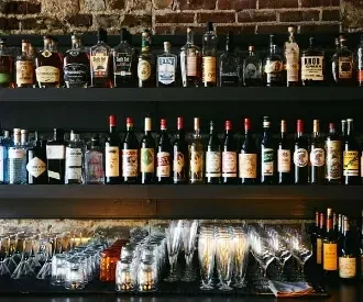 Rustic bar with bottles, various glassware on counter, brick wall.