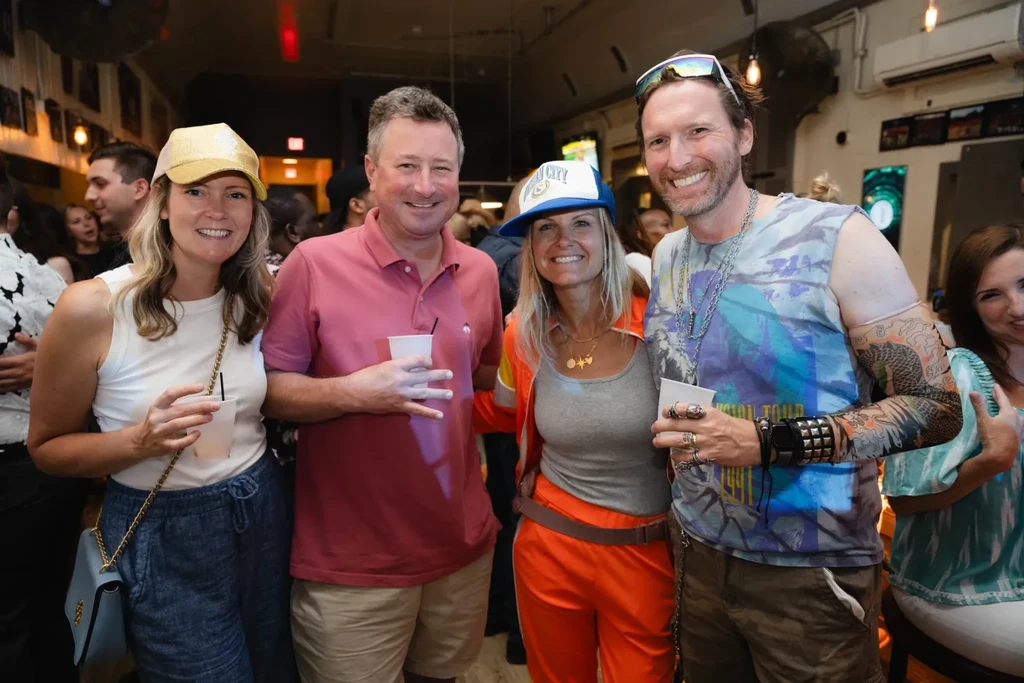 Four smiling people hold cups in a bar.