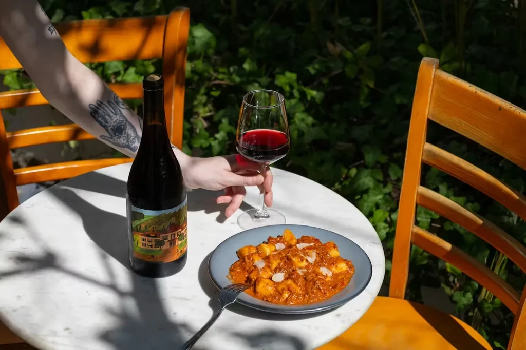 Outdoor dining with gnocchi, red wine, and a tattooed hand.