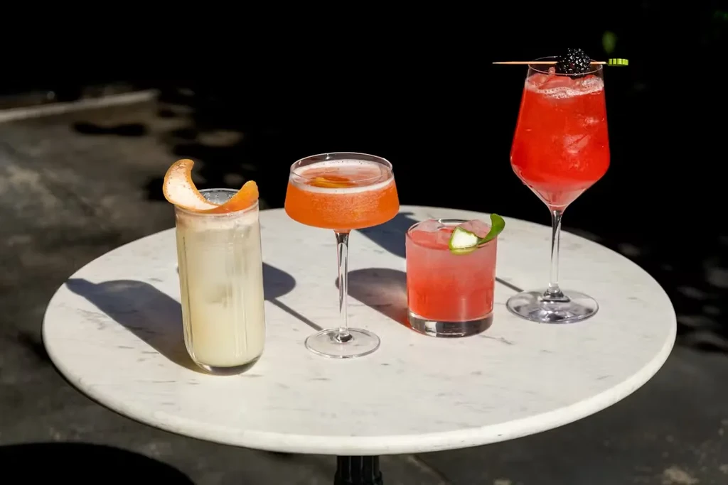 Four colorful, garnished cocktails on a white marble table.