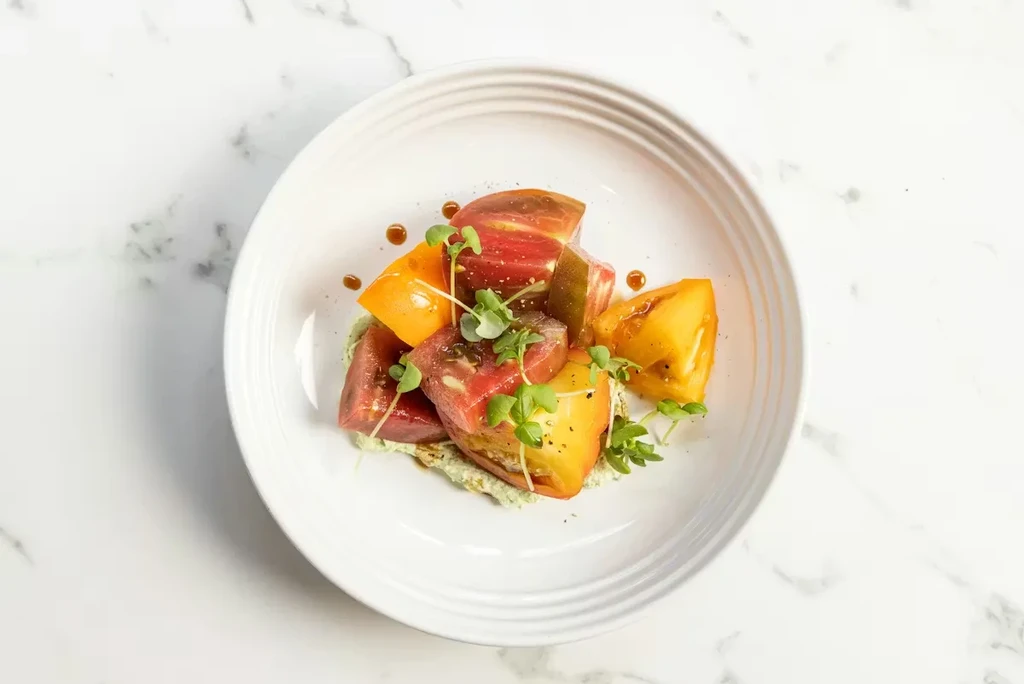 Vibrant heirloom tomato salad with microgreens on a white plate.
