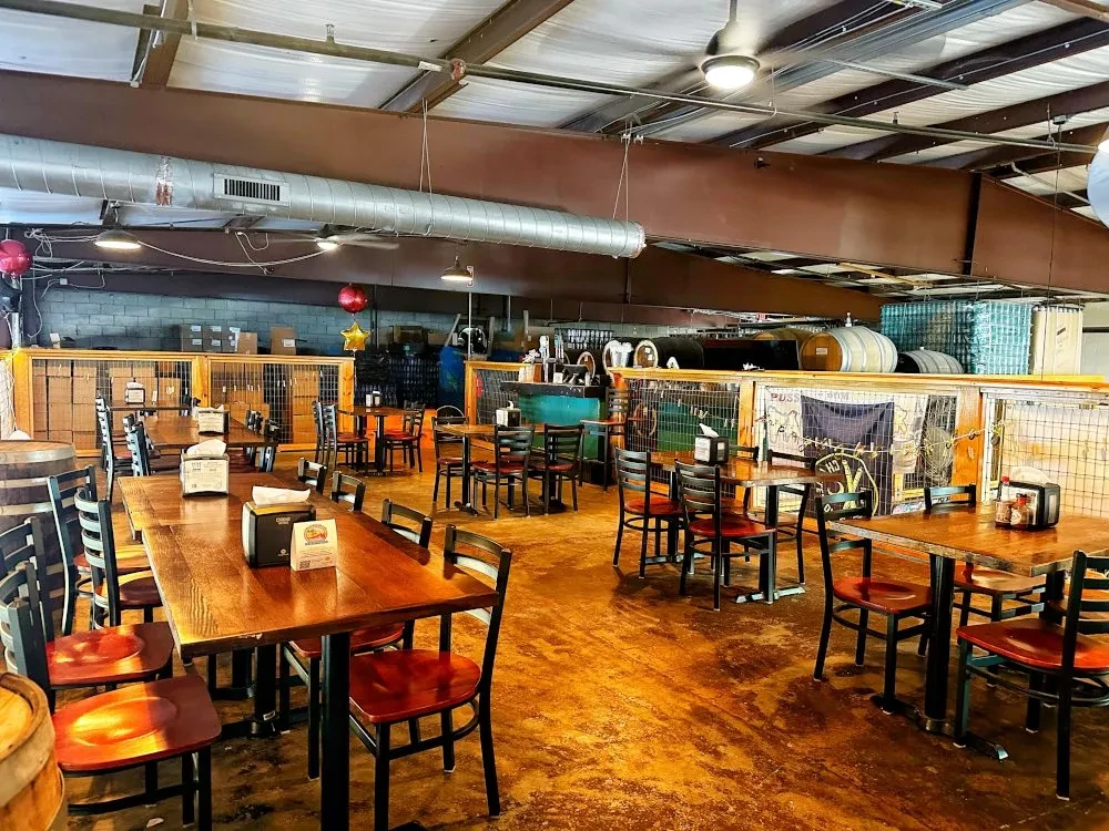 Empty casual restaurant dining, wooden tables, industrial ceiling, bar.