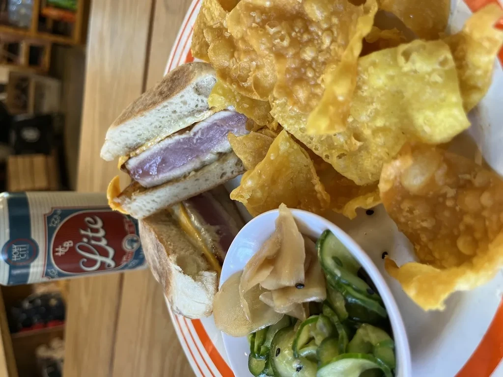 Tuna sandwich, chips, pickled vegetables, and beer on a wooden table.