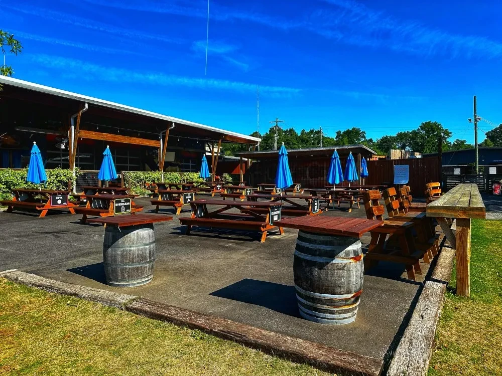 Empty outdoor restaurant patio with wooden tables and blue umbrellas.