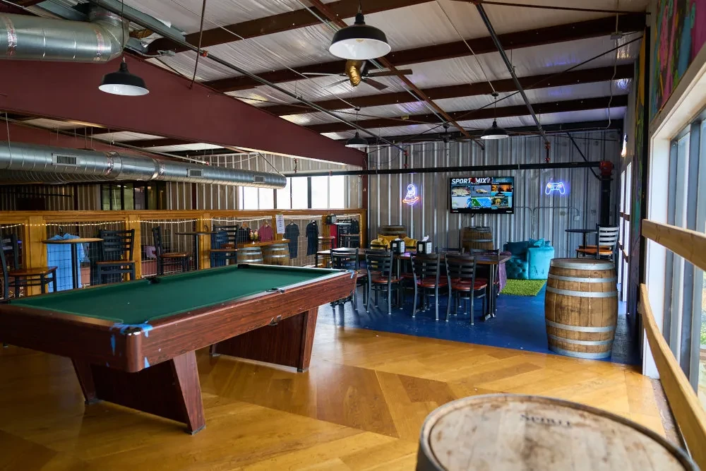 Spacious, industrial bar with pool table, seating, and entertainment area.