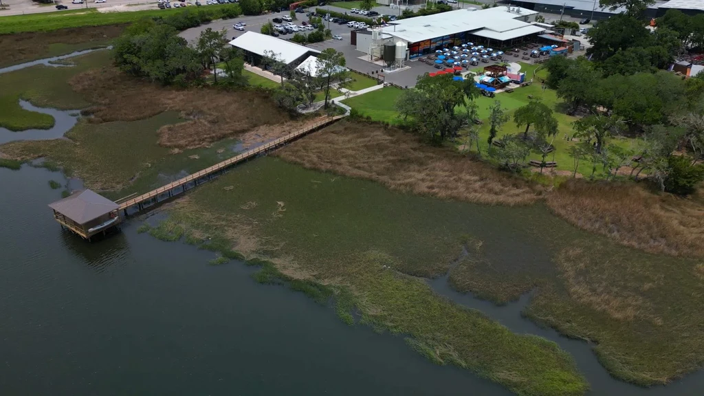 Aerial view of waterfront restaurant, outdoor dining, and pier over marshland.