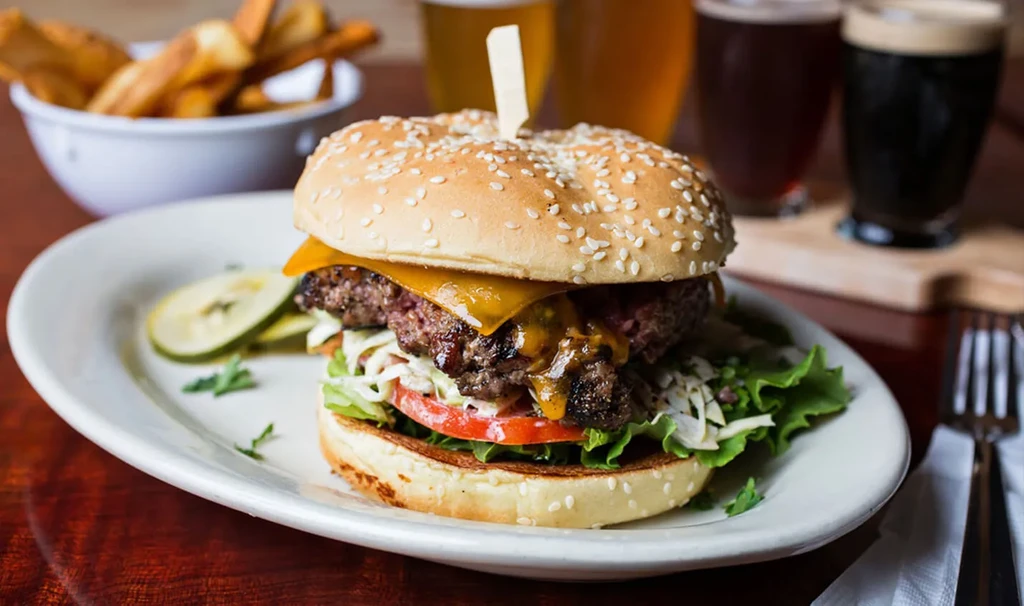 Cheeseburger with melted cheese, fries, and two beers on a table.