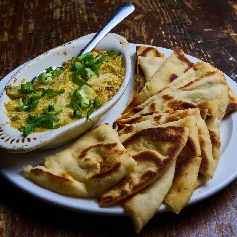 Creamy dip with green onions and toasted flatbread on a wooden table.