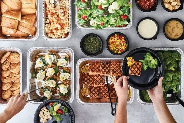 Overhead view of a diverse food buffet with hands serving dishes.