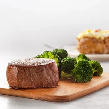 Thick steak, green broccoli, and baked potato on a cutting board.