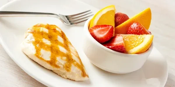Grilled chicken breast and a bowl of strawberries and orange slices.