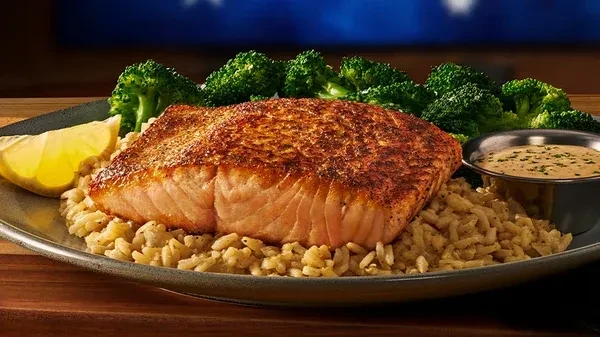 Close-up of cooked salmon, rice, broccoli, lemon, and sauce.