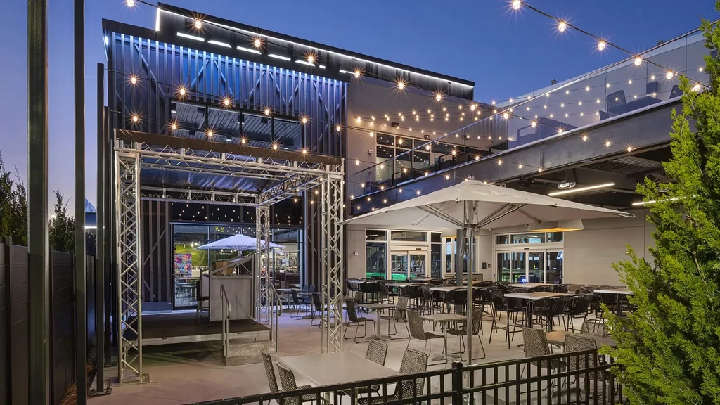 Modern restaurant patio at dusk with string lights and blue accents.