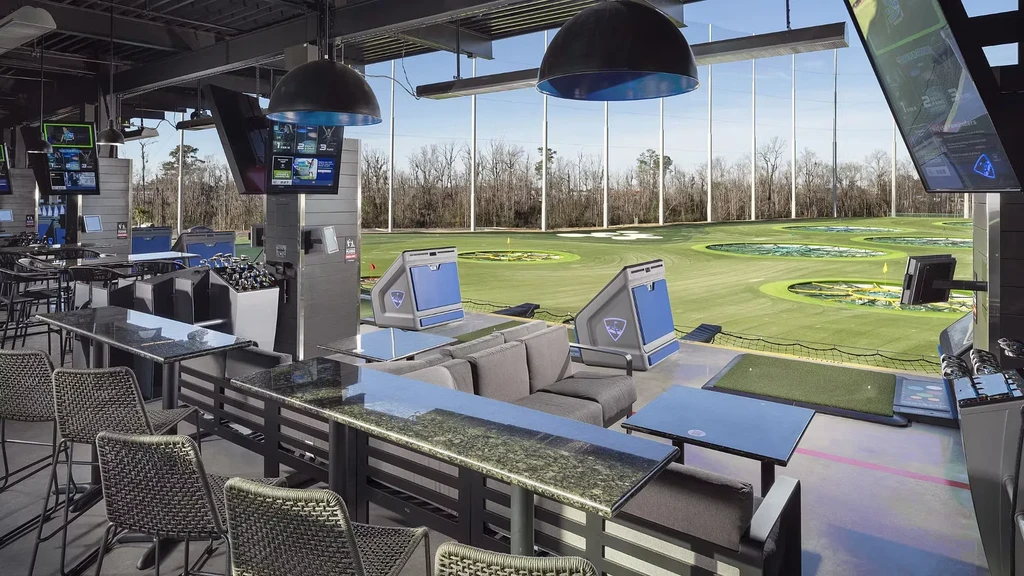 Modern Topgolf interior with restaurant, golf bays, and outdoor driving range.