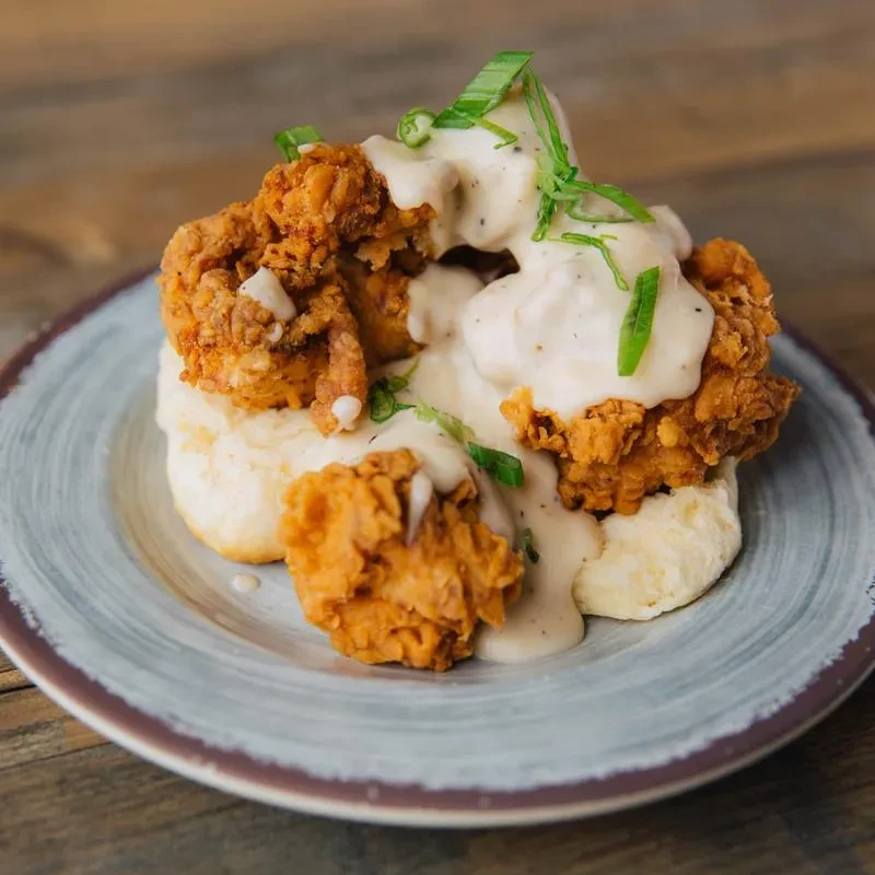 Fried chicken and biscuits smothered in gravy, garnished with green onions.