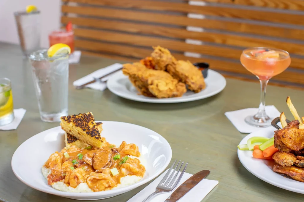 Restaurant table with shrimp and grits, fried chicken, and drinks.