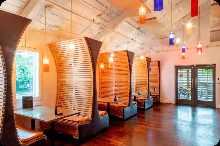 Modern restaurant with high-backed wooden booths and colorful pendant lights.