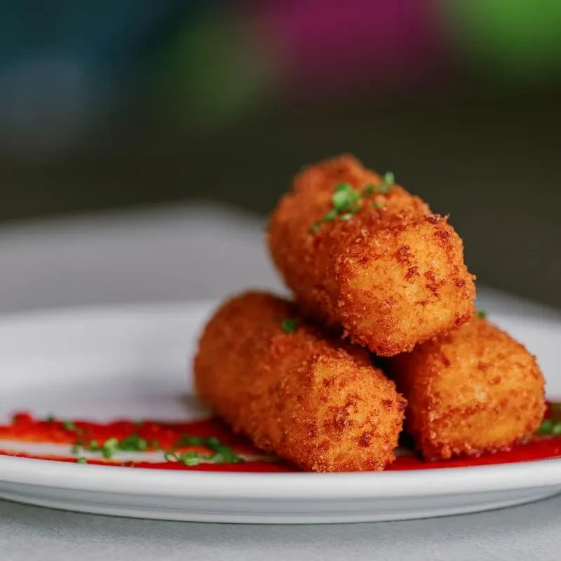 Three stacked golden-brown fried croquettes with red sauce and green herbs.
