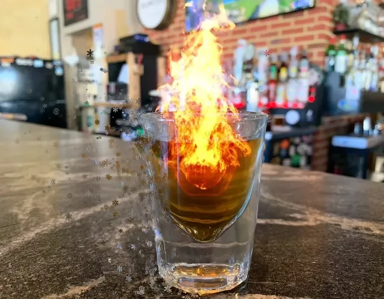 Flaming amber cocktail in a double-walled glass with snowflakes on a bar.
