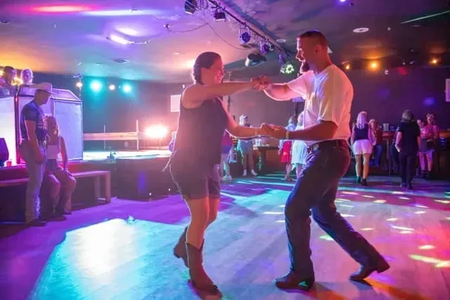 Smiling couple dancing on a vibrant, colorful nightclub dance floor.