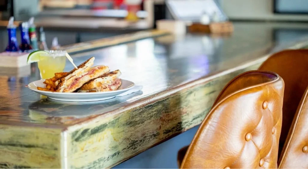 Grilled sandwich, fries, and margarita on a distressed metallic bar counter.