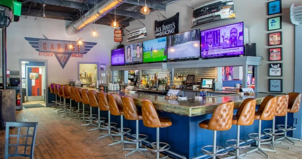 Garage-themed sports bar interior with a long bar, TVs, and stools.