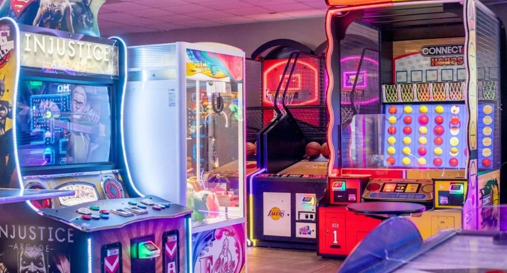 Brightly lit arcade interior featuring fighting, claw, and basketball games.