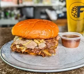 Pulled meat sandwich with melted cheese, caramelized onions, dipping sauce, and beer.