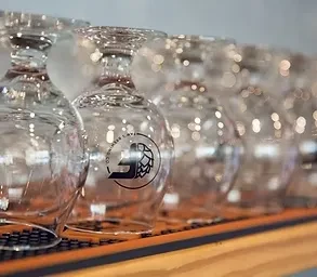 Inverted empty stemmed glasses, one with 'JD' hop logo, on a bar mat.