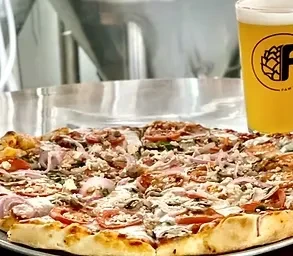 Rectangular pizza, amber beer, and brewery equipment in the background.