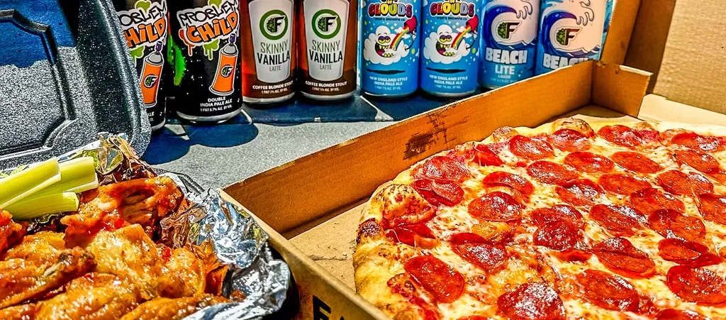 Takeout pepperoni pizza, chicken wings, and assorted craft beer cans.