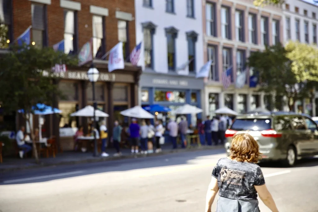 Lively urban street with outdoor dining, brick buildings, and many people.