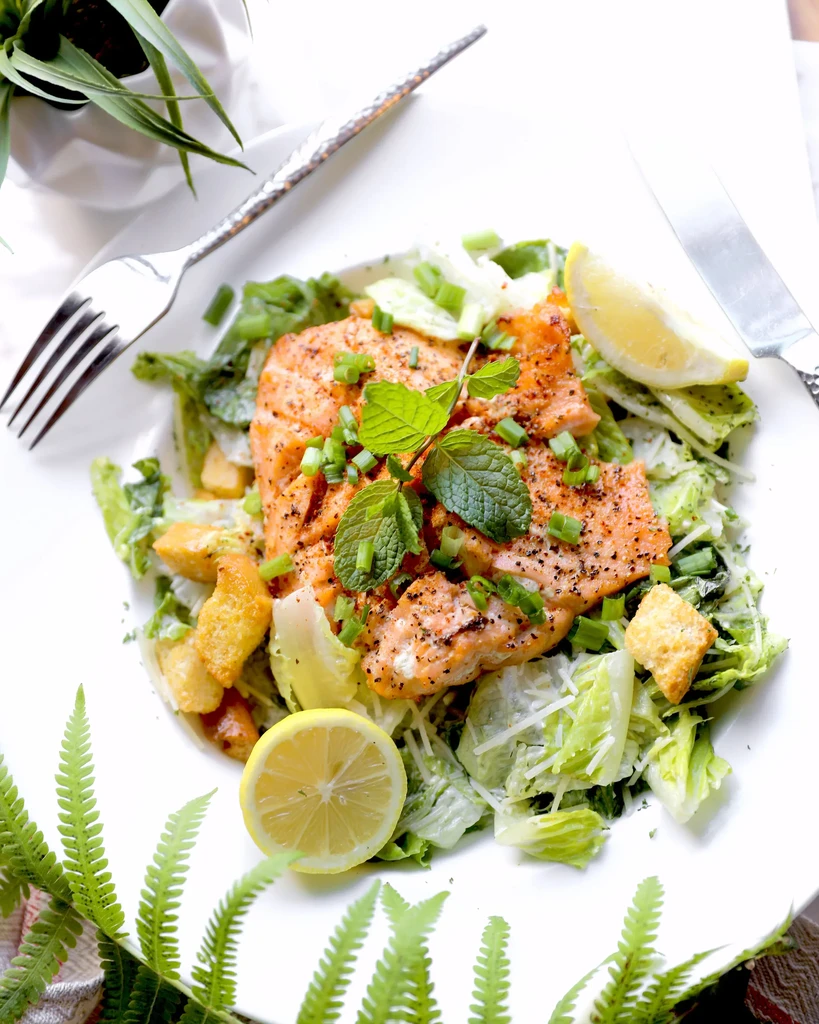 Overhead view of a plated salmon Caesar salad with lemon.