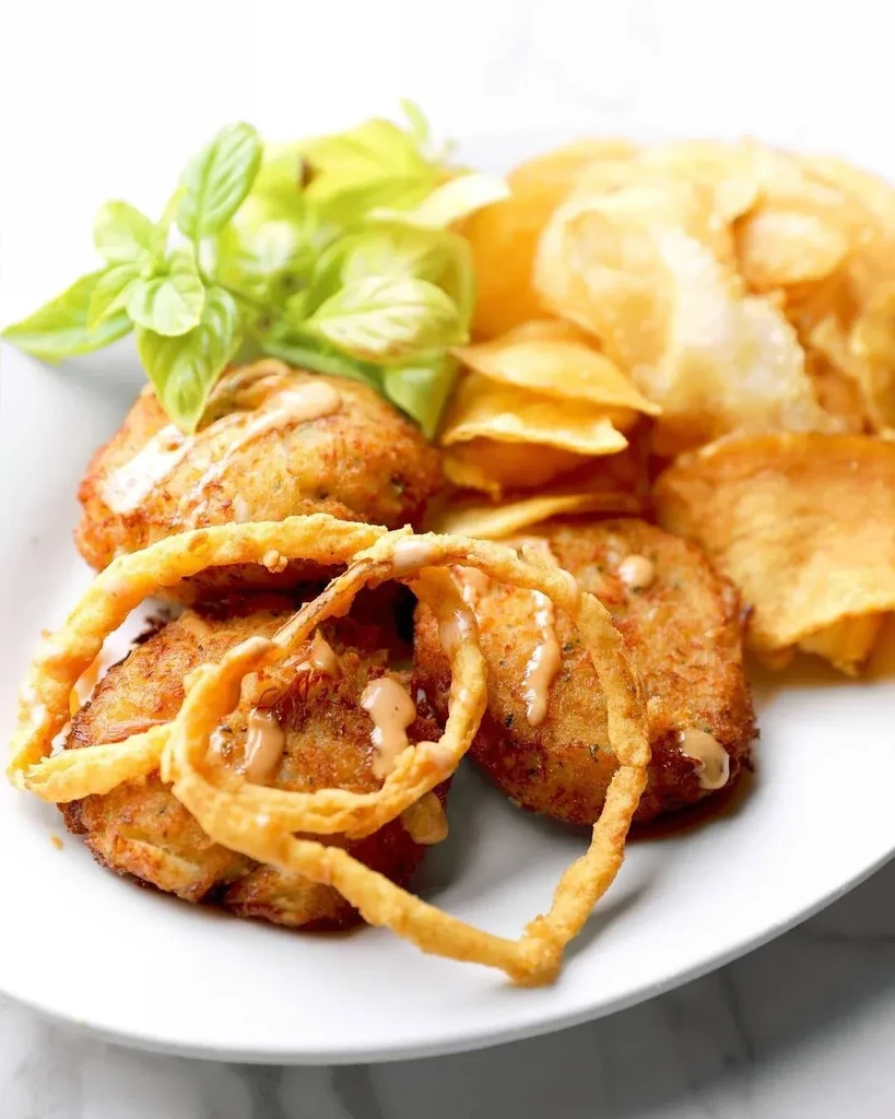 Plate of golden fried patties, chips, onion rings, and sauce.