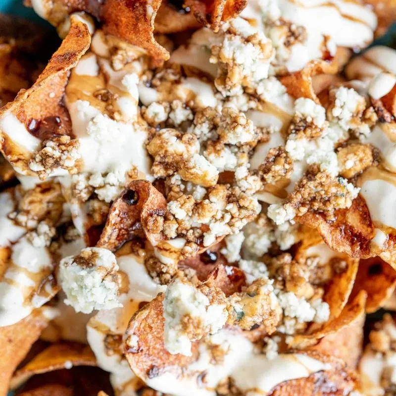 Loaded potato chips topped with creamy sauce, blue cheese, bacon, and drizzle.