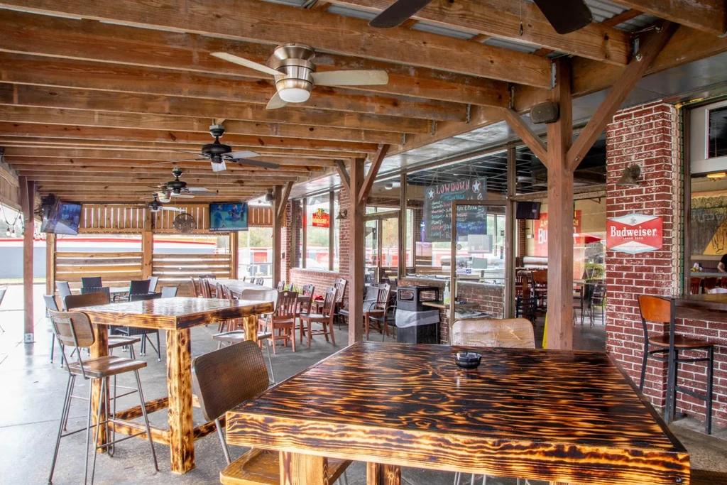 Rustic outdoor dining area with wooden tables under a beamed roof.