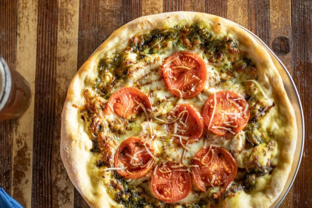 Freshly baked pesto pizza with tomatoes and cheese on a wooden table.