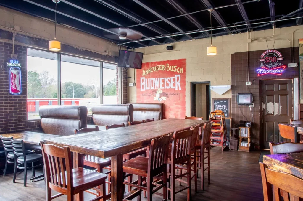 Interior of an industrial-rustic bar with communal seating and Budweiser signs.